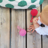 Ein Baby liegt bäuchlings auf einem Holzboden, vor ihm zwei Häkelbälle mit Schlaufen in rot und rosa von Kokomoo.