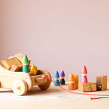Ein kleiner Nachziehwagen aus Holz beladen mit Bausteinen aus Holz, rundherum sind bunte Zwerge von Grapat verteilt.