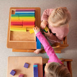 Zwei Kinder sitzen an zwei kleinen Tischen und spielen gemeinsam mit den Holzbausteinen von Glückskäfer.