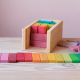 Die bunten Holzbausteine von Glückskäfer liegen flach, farblich sortiert aufgereiht vor der Holzbox, in der weitere Holzbrettchen auf das bespielt werden warten.