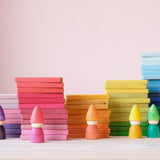 Die 60 bunten Holzbausteine von Glückskäfer sind in fünf Stapeln nebeneinander sortiert aufgestellt. Davor stehen, farblich passend, klein Zwerge Spielfiguren aus Holz.