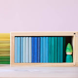 Alle flachen Holzbausteine von Glückskäfer in Blau- und Grüntönen in ihrer Holzbox sortiert aufgereiht, ganz recht ein kleiner grüner Holzzwerg.