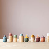 Freies Spielmaterial aus Holz aufgereiht: glatte Becher, gerillte Becher, kleine Holztöpfchen mit Deckel, Filzbälle sind auf den Bechern verteilt.