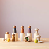 Glatt geschliffene Holzbecher mit Deckel oder ohne Spielfiguren aus Holz in Erdtönen, drei Filzkugeln und zwei kleine Pilz Holzfiguren stehen zusammen oder übereinander.