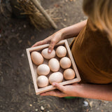 Ein Kind nutzt die kleine Holzbox von Grapat als Tablett und trägt neune Eier, die gerade gut rein passen.