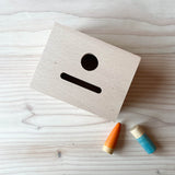 Die Grapat "Permanence Box" für Montessori Beschäftigung mit einem Loch und einem Schlitz im Deckel zu sehen von oben, daneben zwei Grapat Spielfiguren.
