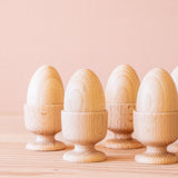Vier Holzeier in Eierbechern aus Holz zum Spielen nebeneinander aufgestellt.