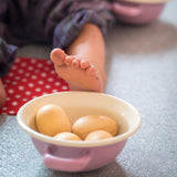 Vier Eier aus Holz liegen in einer Schüssel aus Emaille, dahinter ist die Fußsohle eines Kleinkindes zu sehen, die an den Rand der Schüssel stoßt.