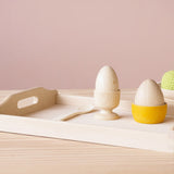 Frühstück am Tablett aus der Puppenküche: Es gibt Holzei im Eierbecher und in einem gelben Schälchen von Grapat, daneben liegt ein kleiner Holzlöffel.