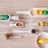 Das 6er-Set Holzlöffeln und Holzschaufeln von Kokomoo: in allen sechs verschiedenen größeren und kleinen Holzlöffeln liegt verschiedenes Material: von einer Walnuss, über Grapat Nins, bis hin zu größeren Holzkugeln und kleinen Holzperlen.