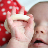 Eine Baby hält einen Holzring in der Hand und sieht ihn fasziniert an.