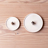 Zwei kleine Holzteller aus Ahornholz, unterschiedliche Größen, liegen nebeneinander. Es liegt jeweils eine Eichel auf den Tellern.