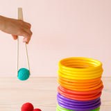 Eine Hand hält die Holzzange, mit der ein türkiser Häkelball von Kokomoo gegriffen wird. Daneben sind bunte Motorikringe aufgestapelt.