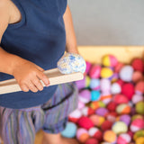 Ein Kind hält einen Häkelball mit der Holzzange von Kokomoo.