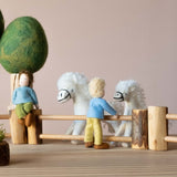 Spielfiguren aus Filz und weiße Filpferde stehen rund um Holzzäune von Drei Blätter.