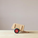 Kleiner Spielzeuganhänger aus Holz von Fagus von der Seite, die Anhängevorrichtung liegt am Boden auf.