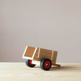 Kleiner Spielzeuganhänger aus Holz von Fagus von der Seite, die Anhängevorrichtung liegt am Boden auf, die Öffnung zum Verladen hinten ist zu sehen.