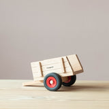 Kleiner Spielzeuganhänger aus Holz von Fagus von der Seite, die Anhängevorrichtung liegt am Boden auf, das Fagus Logo ist zu sehen.