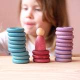 Blaue, rote und lila Holzplättchen und Holzringe aufgestapelt, dahinter ein Kind.