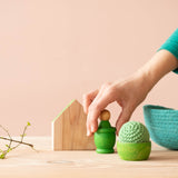 Gruene Grapat Spielmaterialien aus Holz mit einem grünen Häkelball von Kokomoo und einem gruenen Koerbchen. Eine Hand greift nach einem Grapat Nin.