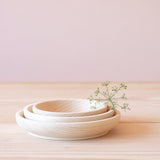 Man sieht ein 3er Holzschalen-Set aus unbehandeltem Holz. Alle 3 Schalen stehen ineinandergestapelt. Eine Bluete liegt darauf.