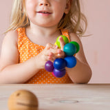 Ein Kleinkind hält den bunten Kugelgreifling in Regenbogenfarben in der Hand und lächelt.