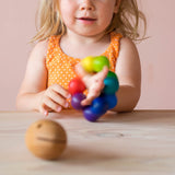 Ein Kleinkind hat den bunten Kugelgreiflingvon Kokomoo am Handgelenk und schüttelt die Hand, zu erkennen, weil der Baby Greifling unscharf ist.