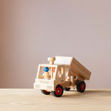 Der LKW-Kipper von Fagus aus Holz, von schräg vorne. Im Führerhaus zwei Spielfiguren aus Holz und die Ladefläche wird gerade gekippt.