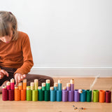 Alle Teile des Grapat "LA" Spielmaterial Sets in Erdtönen nebeneinander und übereinander aufgestellt. Ein Kind sitzt dabei und legt kleine Steine auf die Lola Spielfiguren.
