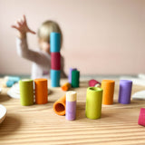 Vorne scharf im Bild stehende Lolas und Becher von Grapat, hinten unscharf ein Kind, das einen Turm aus den Bechern baut.