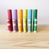 Alle Teile des Lola Erdtöne Sets aufgestapelt, Lolas in drei verschiedenen Größen und 6 verschiedenen Farben, dahinter die 18 Becher in den 6 verschiedenen Farben.