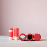 Rote Lola Spielfiguren von Grapat in drei Größen, daneben eine Rohre, ein Becher und ein geschlossener Zylinder ebenfalls in rot.