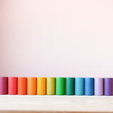 Die bunten Zylinder aus Holz vom Grapat Spielmaterial Lola stehend aufgereiht, farblich sortiert als Regenbogen.