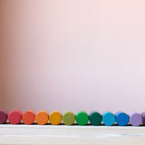 Die bunten Zylinder aus Holz vom Grapat Spielmaterial Lola liegend aufgereiht, farblich sortiert als Regenbogen.