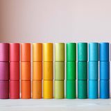 Die bunten Röhren, Becher und Zylinder aus Holz vom Grapat Spielmaterial Lola stehend aufgereiht, farblich sortiert nach dem Regenbogen.