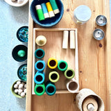 Ein Holztablett mit verschiedenen freien Spielmaterialien darauf: Grapat Lola, kleine Klangschalen, Holzringe und vieles mehr.