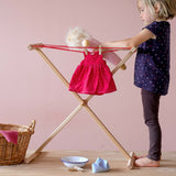 Das rote Tupfenkleid der Stoffpuppe Lotti hängt auf der kleinen Wäscheleine für Kinder, ein Kind legt auch die Puppe auf die Wäscheleine.