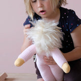 Ein Kind spielt mit der weichen Stoffpuppe Lotti rot, die ihr Kleid ausgezogen hat, der rosa Frottee des Puppenkörper ist zu sehen und die weißen Mohairhaare.