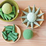 Grapat "Green Cone", Mandale Steine in Kegelform und drei Häkelbälle von Kokomoo liegen in Holztellern und einem Jutekorb, teilweise chaotisch, teilweise zu einer Sonne gelegt.