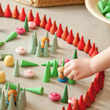 Ein Kinderhand baut eine kleine Märchenlandschaft mit vielen verschiedenen Mandala Steinen aus Holz in verschiedenen Farben und Formen.