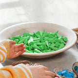 Ganz viele Grapat "Green Cone", also grüne Mandala Steine in Kegelform liegen in einer großen Schale aus Holz, eine Kinderhand greift danach.
