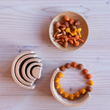 Ein Blick von oben auf einen Grimms-Naturholz-Regenbogen, eine Holzschale und kleine Mandala Holzkürbisse von Grapat in Orange, Gelb und Brauntönen.