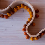 Aus aneinandergereihten Naturholzbögen wurde die Form einer Schlange gelegt. Man sieht von oben drauf. An die Holzbögen gereiht, stehen kleine Holzkürbisse in Orange-Tönen.