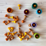 Ein Blick von oben auf eine Holzfläche. Darauf liegen verteilt kleine orange-gelb-braune Kürbisse aus Holz. Es stehen 6 Holzbecher in Erdfarben - darin befinden sich auch diese kleinen Kürbisse.