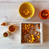 Ein Bllick von oben auf eine Holzfläche. Man sieht ein kräftig gelbes Jutekörbchen, darin liegen 3 kleine Holzkürbisse. Daneben steht eine orange Holzschale - mit 2 orangen Kürbissen. Eine quadratische, flache Holzbox beinhaltet viele dieser Kürbisse.