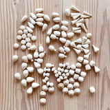 120 kleine Mandala Spielsteine aus naturbelassenem Holz in verschiedenen Formen von Grapat liegen verstreut auf dem Holzboden.