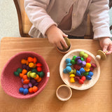 Die 36 Stück Mandala Pilze von Grapat "Mushrooms Rainbow" verteilt in einem Körbchen und einer Holzschale. Ein Kind spielt damit.