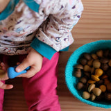 Ein Kind hält blaue Mandalasteine, neben ihm steht ein blauer Jutekorb mit braunen kleinen Pilzen aus Holz.