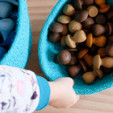 Ein Kind greift nach einem lauen Jutekörbchen gefüllt mit vielen braunen Holzpilzen zum Spielen.