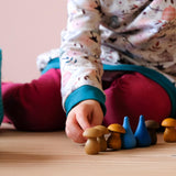 Ein Kind stellt blaue "Regentropfen" Mandalasteine und braune Holzpilze Mandalas in einer Reihe auf.